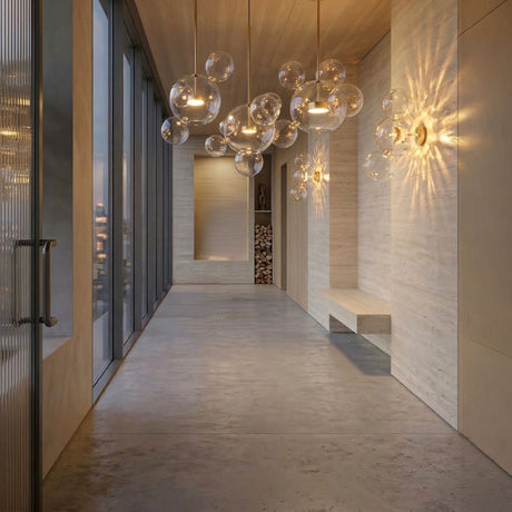 Niori Bubble 3 Light LED Glass Linear Pendants in gold illuminate a modern hallway with travertine walls, a built-in bench, and floor-to-ceiling windows.
