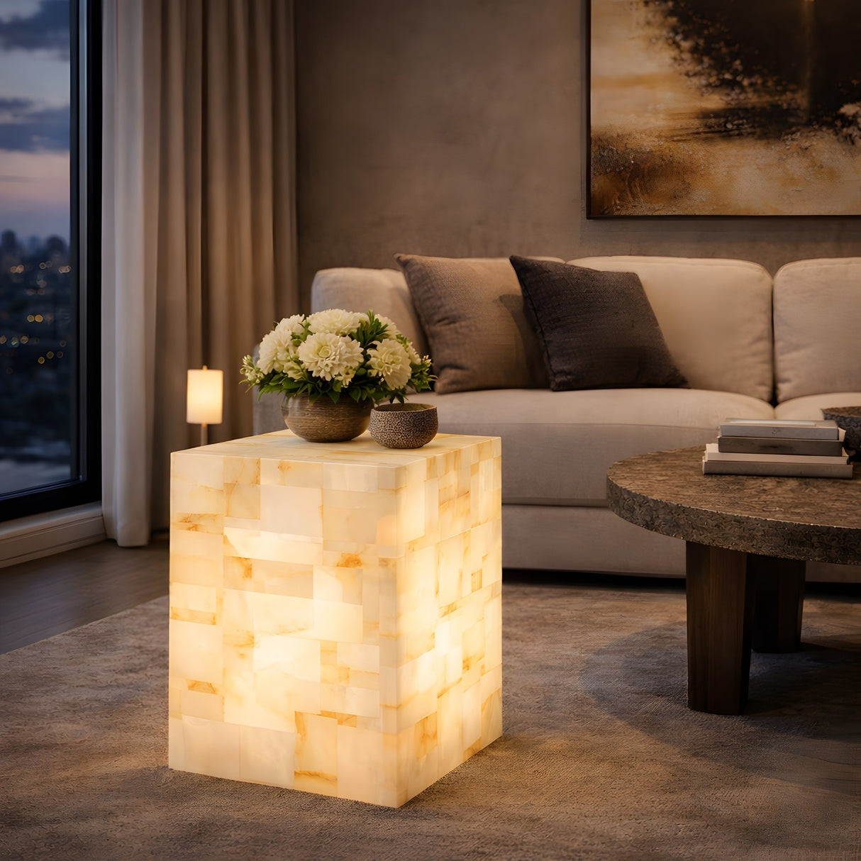 The Stratare 2 Light Large Stratified Alabaster Floor Lamp – Soft White, with a marble-like pattern, stands beside a round coffee table in a modern, cozy living room featuring a beige sofa, cushions, flowers, and a large window.