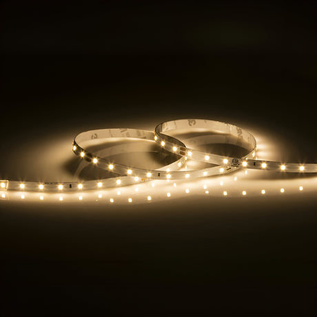 The 24V LED Strip Light 3000K - 5m emits a soft, warm white glow against a dark backdrop. This dimmable strip gently curves, casting a cozy ambiance over the surrounding area.
