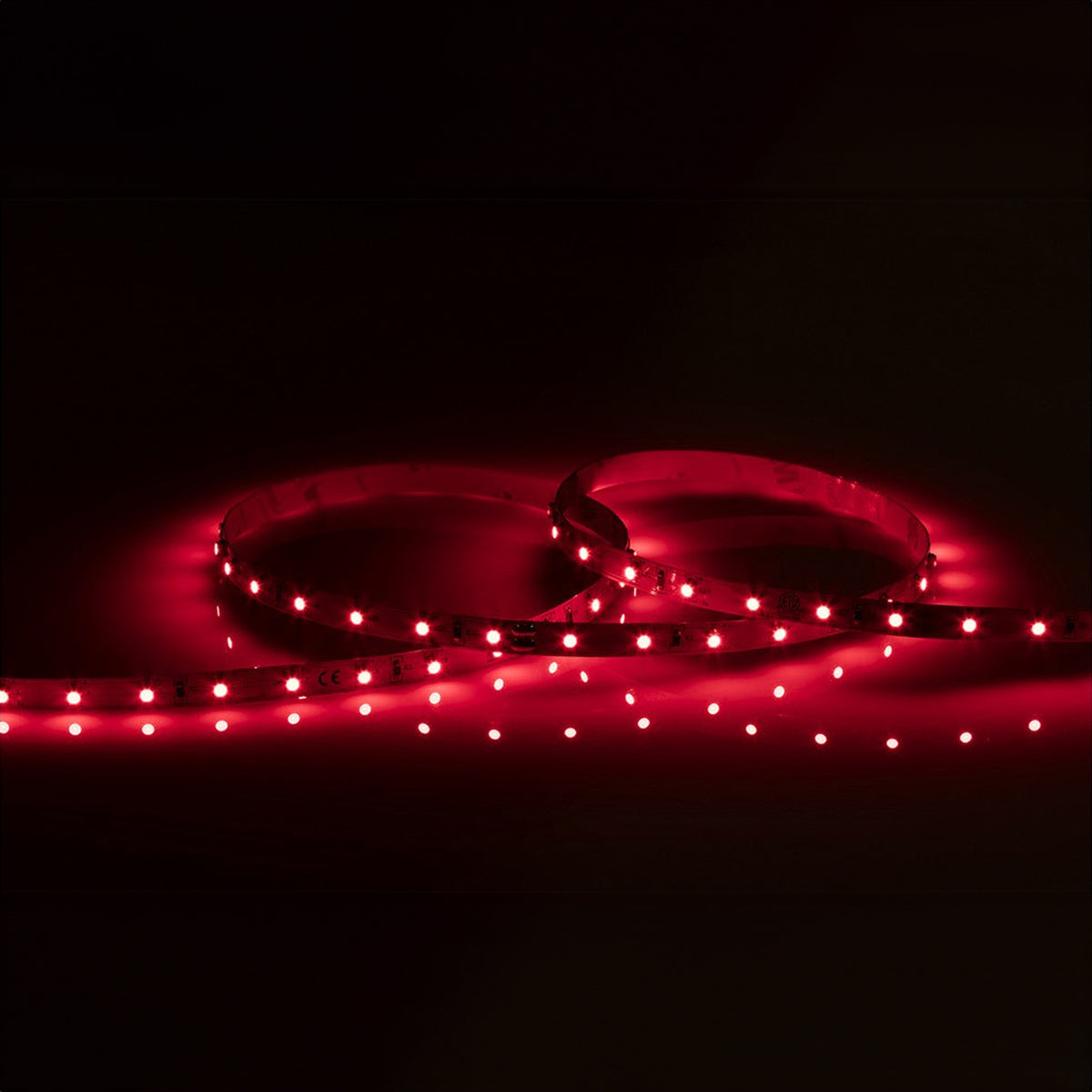 Two loops of the 24V Red LED Strip Light - 5m emit a warm red glow in a dark setting, casting vibrant illumination. Arranged in a circular pattern, these strips highlight the intensity and brightness attributed to their IP20 rating.