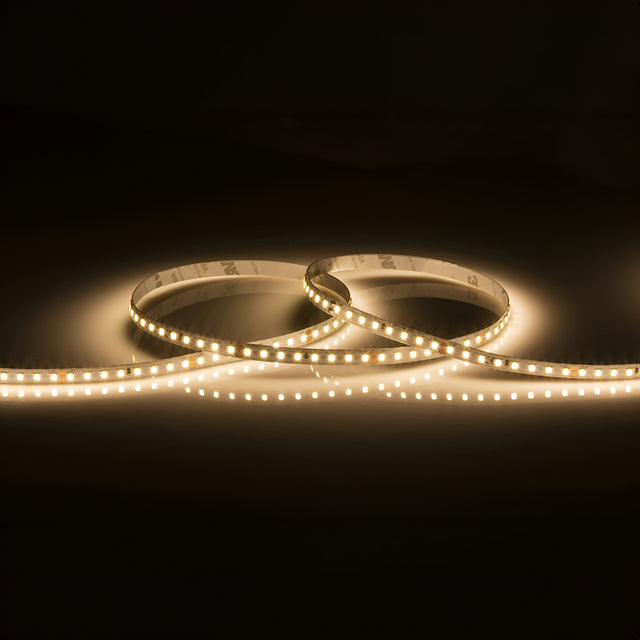 The 24V High Lumen LED Strip Light 3000K - 5m emits a soft glow against a dark background, casting a warm illumination on the surface beneath.