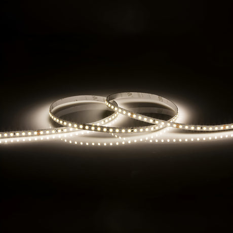 A coiled strip of the 24V High Lumen LED Strip Light 4000K - 30m shines brightly against a dark background. This versatile lighting solution offers warm white illumination, while also providing the flexibility to shift to cool white for a crisp ambiance, delivering soft and even lighting.