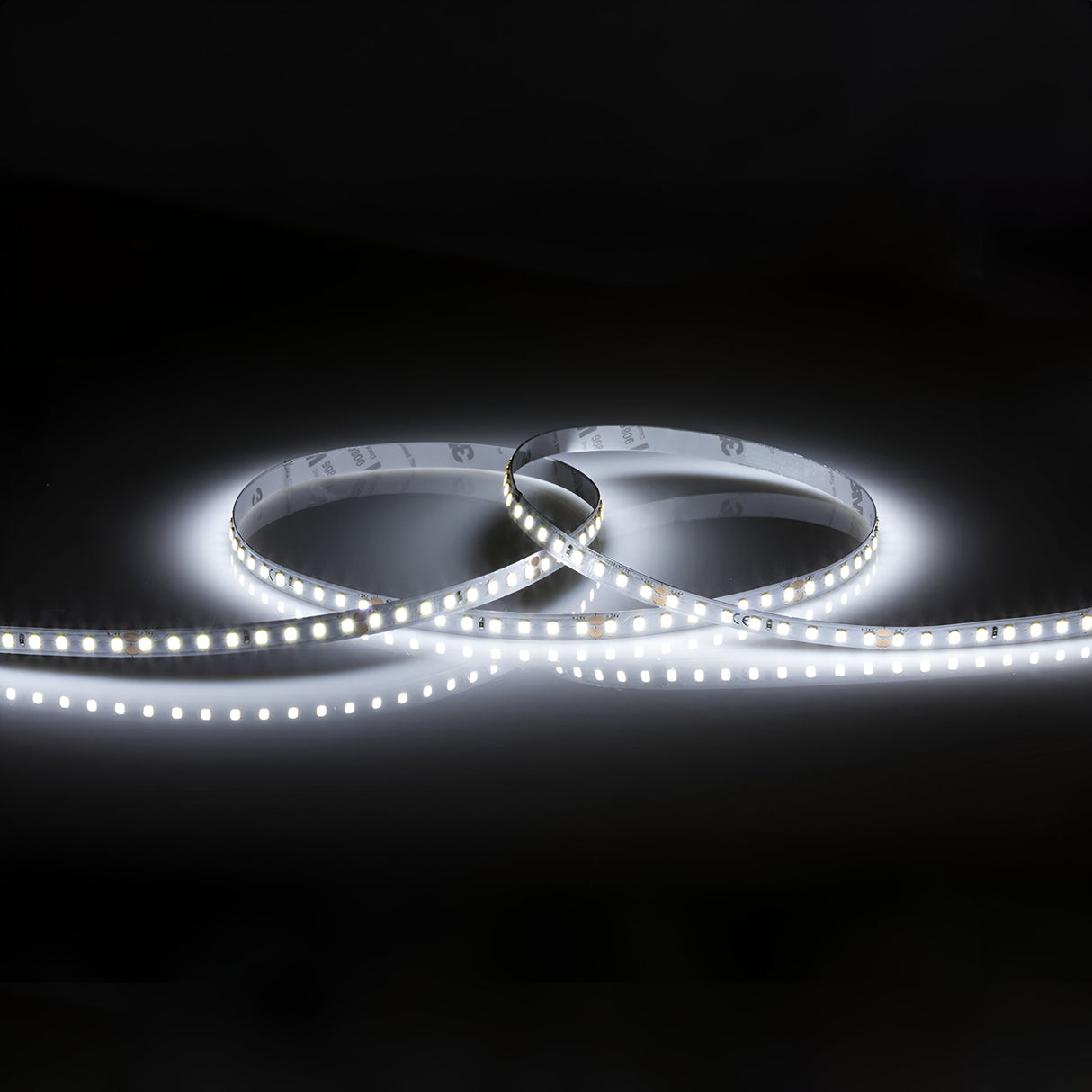 The 24V High Lumen LED Strip Light 6000K - 30m is arranged in loops against a dark background, showcasing its dimmable lighting features. It emits a bright, cool white glow that highlights its numerous tiny bulbs.
