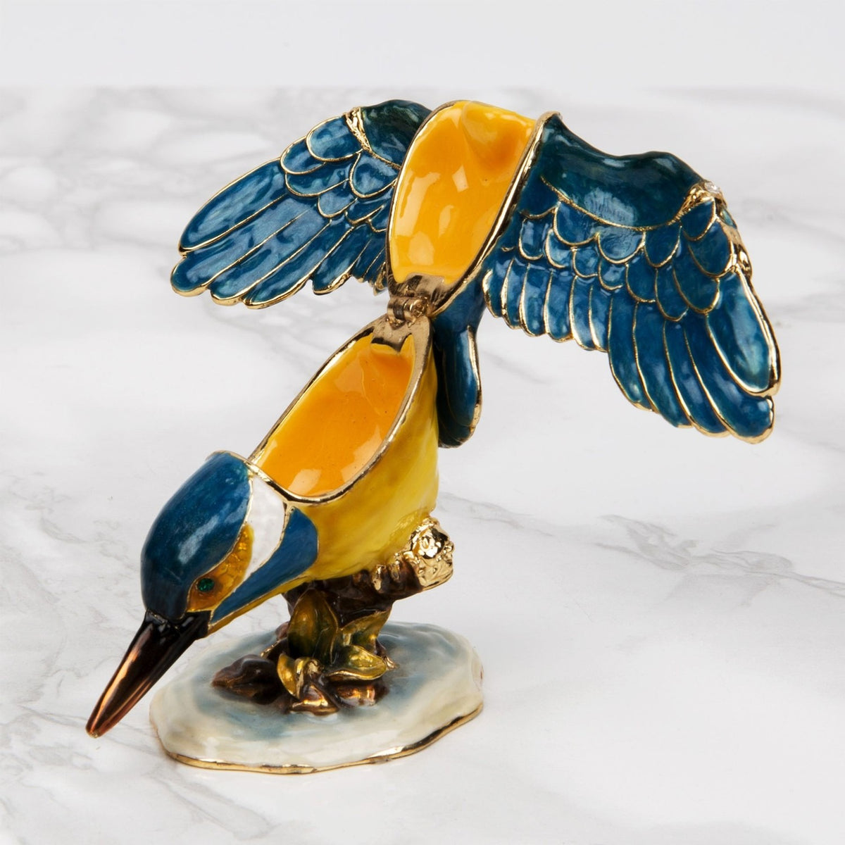 Perched Kingfisher Metal Trinket Box with hinged wings open, revealing a yellow-orange interior, blue and gold enamel feathers on a white marbled surface.