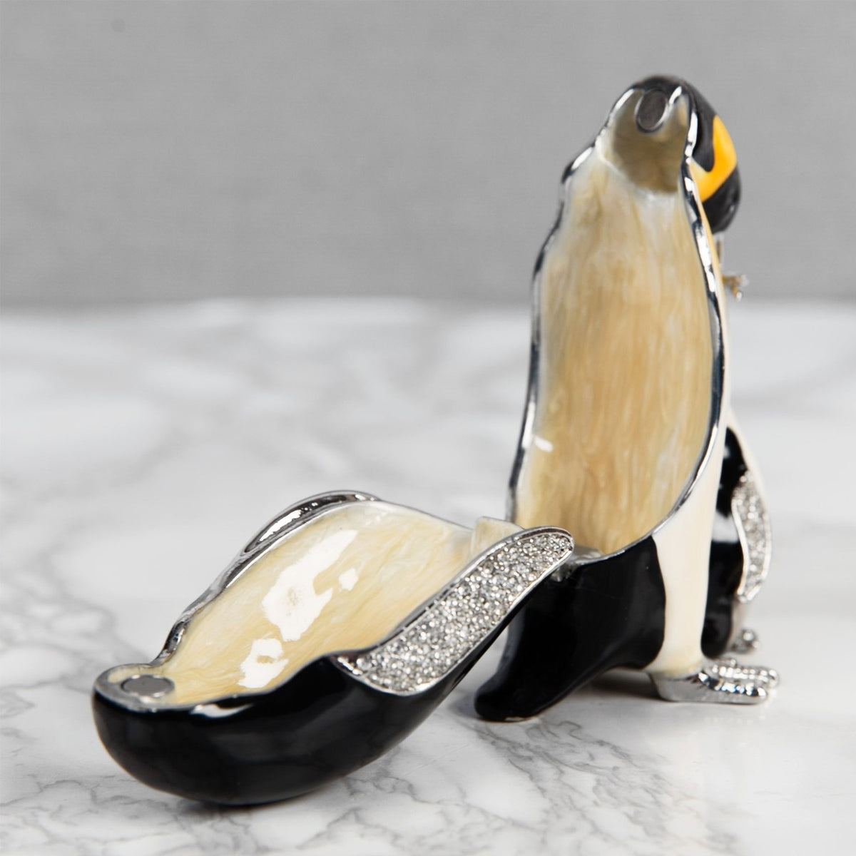 Penguin & Chick handpainted metal trinket box shown open, revealing a cream-toned interior with glittered silver trim, black and white exterior, on a marble surface.