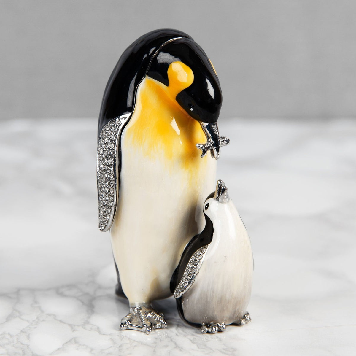 Penguin & Chick handpainted metal trinket box in black and white with yellow-washed chest, crystal-set silver-tone wings and feet, shown on a light marble surface.