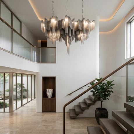 Modern, minimalist foyer with the Valora 15 Light Metal Chain Veil Suspension Light in Nickel, floating wooden staircase, large windows, potted plant, and a built-in wooden display shelf; neutral palette and abundant natural light fill the space.