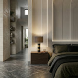 Modern bedroom with a dark wooden nightstand, the Arvella 1 Light Striped Marble Table Lamp in black & gold, green bedding, textured wall panels with soft lighting, marble floor, and an open hallway with built-in shelves and large windows.