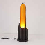 The Stealth Table Lamp - Brass & Black features a sculptural, minimalist design with a sleek black base and tall brass-colored fixture, emitting a warm glow. Its visible power cord adds modern flair—perfect for contemporary decorative lighting.