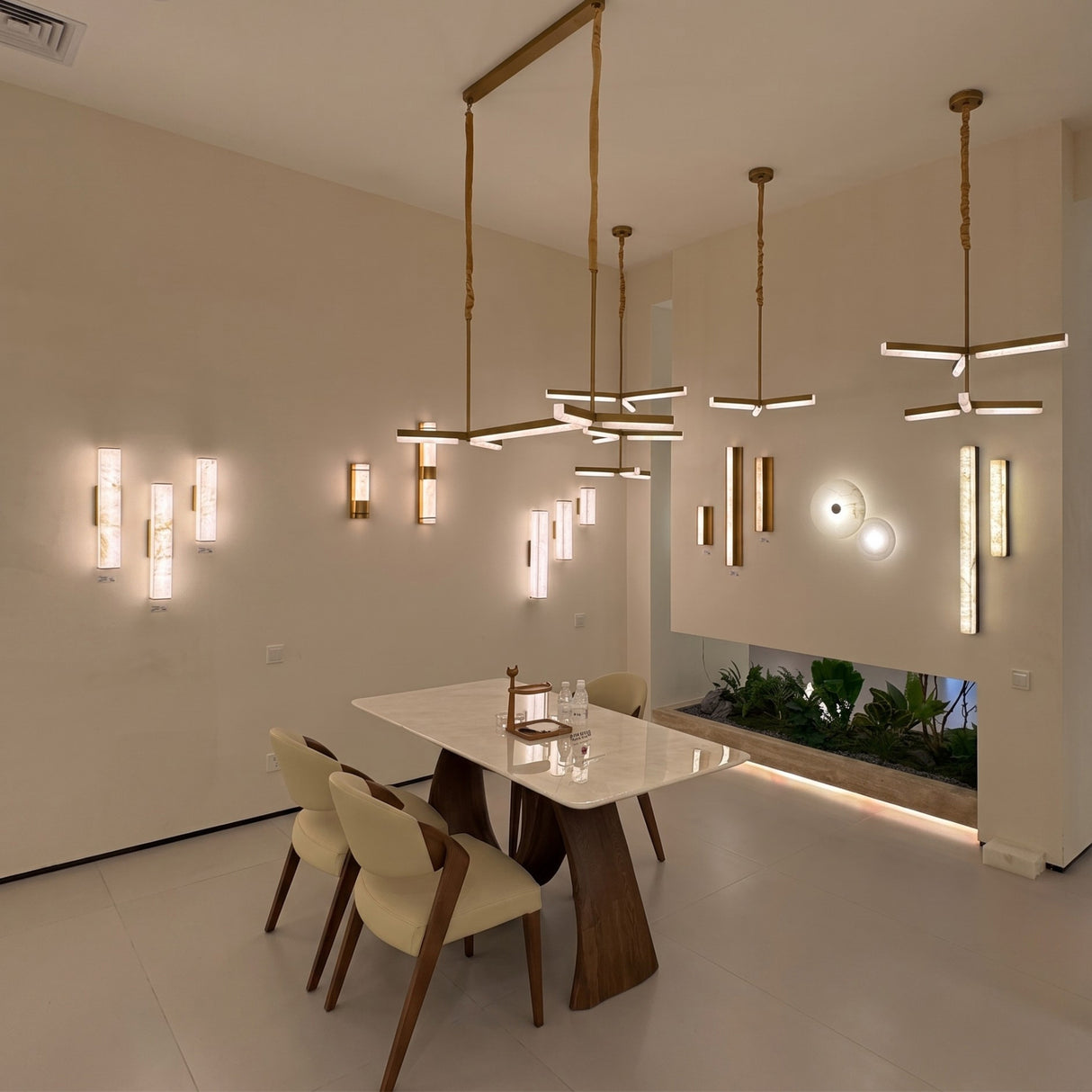Elvaris LED Small Vertical Alabaster Wall Light in Brushed Brass shown among other pendant and wall lights in a dining room setting with marble table and chairs.