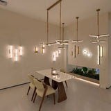 Elvaris LED Small Vertical Alabaster Wall Light in Brushed Brass shown among other pendant and wall lights in a dining room setting with marble table and chairs.