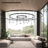 Skybell Circle Iron Ring LED Pendant Light in Ebony Black, nested round rings with cone-shaped heads on slim stems, shown above a grey sectional sofa in a living room.