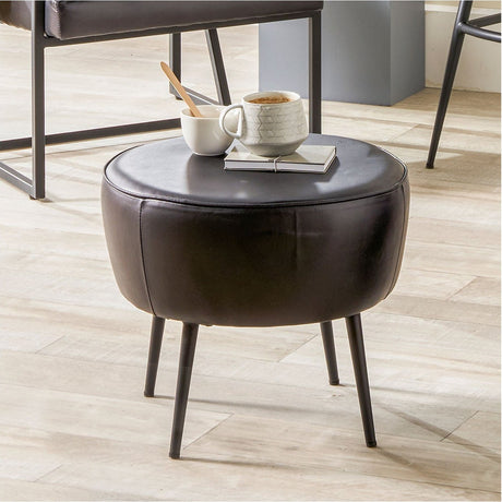Donato Black Leather & Iron Stool - 38cm with a round padded seat and slim splayed iron legs, shown in a living room used as a side table with mugs and a notebook.