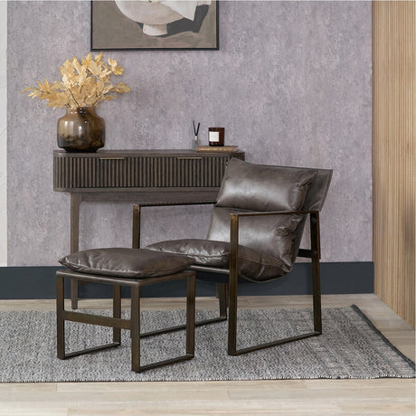 Nico Peppercorn Leather Chair & Footstool with cushioned seat, angled bronze-tone metal frame and matching footstool, styled in a room with a wooden console and rug.