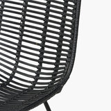 Close-up of the Black Rattan Core & Iron Dining Chair, showing woven rattan strands in a curved seat with black metal frame detail, set against a plain white background.