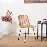 Rattan Core & Black Iron Dining Chair with woven natural rattan seat and back on slim black metal legs, shown in a room setting beside a patterned vase and side table.