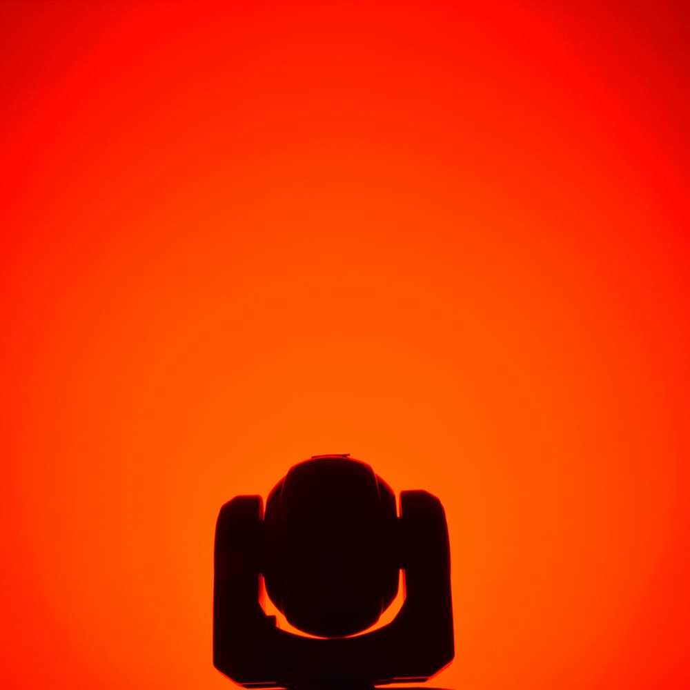 QTX 80W RGBWA COB LED moving head light by AVSL, silhouetted head and yoke against a saturated red-orange background.