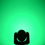 QTX 80W RGBWA COB LED moving head light by AVSL, silhouetted head and yoke shown from the front against a saturated green wash background.