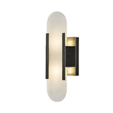 The Lirone 1 Light Small Vertical Capsule Alabaster Wall Light in soft white and black features an oval alabaster shade with two vertical black accents on a rectangular base, providing gentle, diffused lighting for modern interiors.