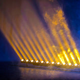 AVSL QTX 24x3W LED Wall Wash Bar in matt black, projecting amber beams and haze upward from its row of lit emitters against a blue backdrop.