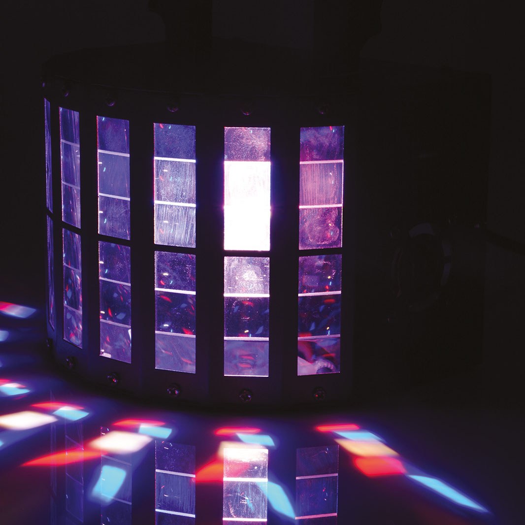 QTX Derby9 LED derby light effect by AVSL, matte black cylindrical housing projecting purple, red and blue rotating beam patterns across a dark floor.