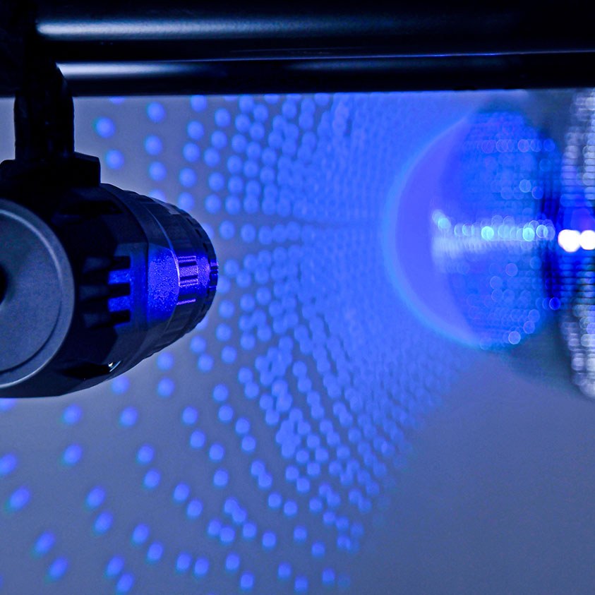 QTX 10W RGBW LED spotlight by AVSL mounted on a bracket, projecting a tight blue beam onto a mirror ball with scattered dot reflections.