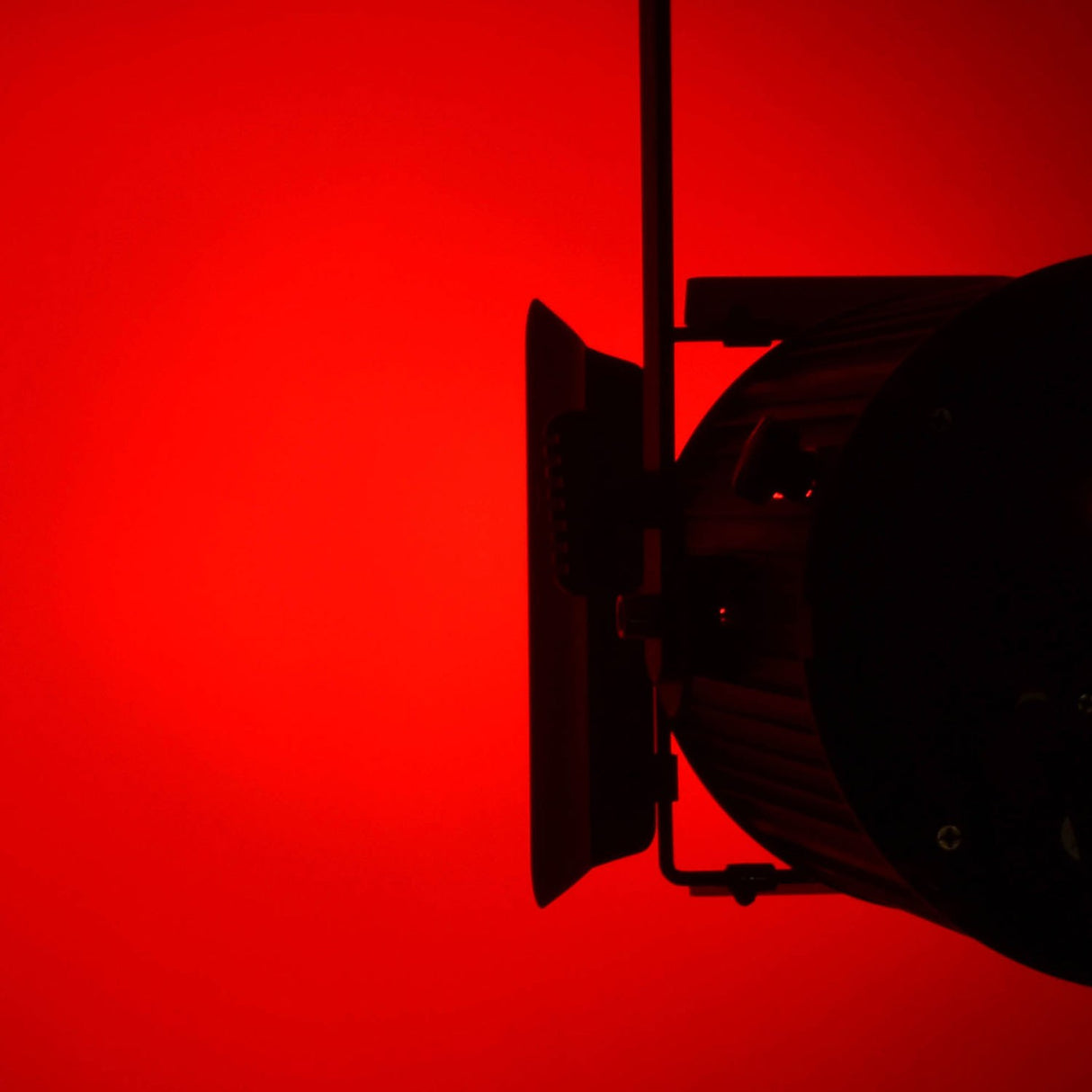 Citronic MFZ160-RGBW mini Fresnel zoom LED stage light shown from the side with barn doors, lit red against a red background.