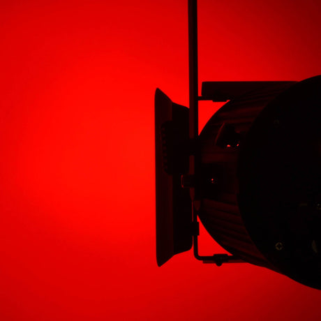 Citronic MFZ160-RGBW mini Fresnel zoom LED stage light shown from the side with barn doors, lit red against a red background.