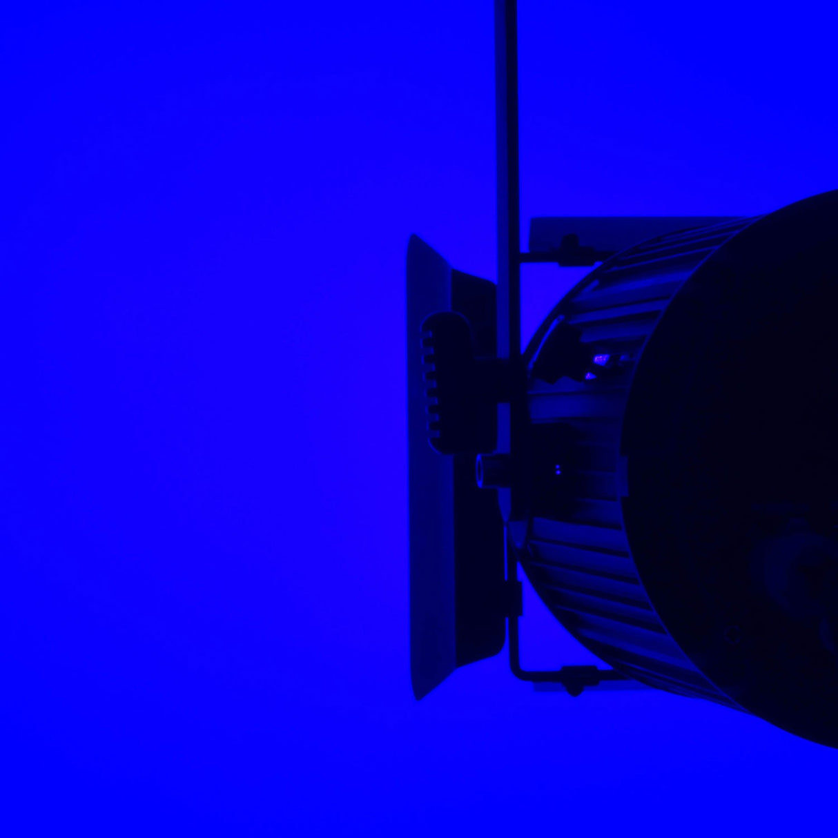 Side view of the Citronic MFZ160-RGBW 160W Mini Fresnel Zoom LED Light with barn doors and mounting bracket, lit against a deep blue background.
