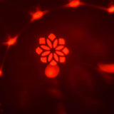 AVSL QTX Crystal Blaze RGBW tabletop LED light effect projecting a red floral GOBO pattern with scattered beams across a dark surrounding area.