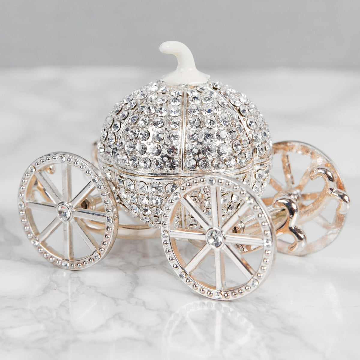 Crystal pumpkin carriage hinged trinket box in silver metal, with crystal-covered curved panels, a white stem top, and four spoked wheels, shown on a marble surface.