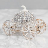 Crystal pumpkin carriage hinged trinket box in silver metal, with crystal-covered curved panels, a white stem top, and four spoked wheels, shown on a marble surface.