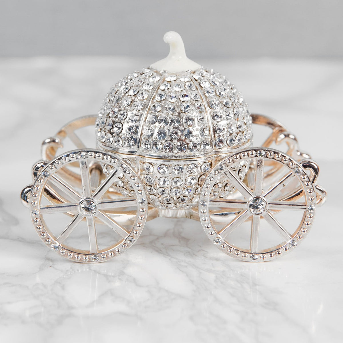 Crystal Pumpkin Carriage Hinged Metal Trinket Box in silver, with crystal-covered curved panels, a white stem top, and four spoked wheels, shown on a plain marbled background.
