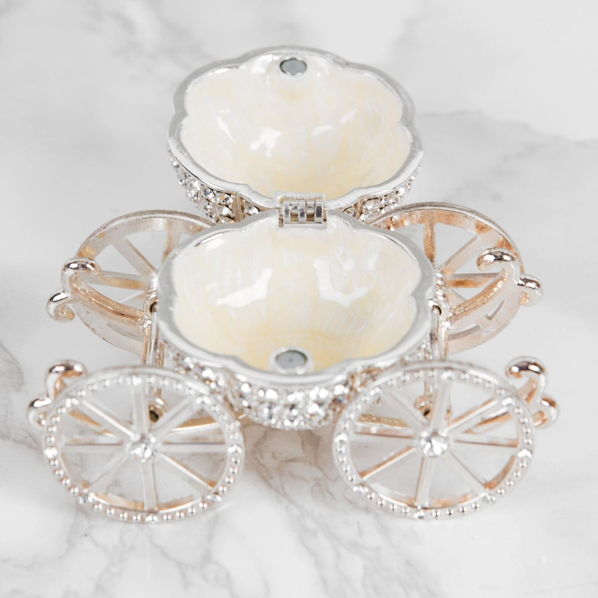 Crystal Pumpkin Carriage hinged trinket box in silver metal, open lid revealing two cream enamel compartments, set on crystal-studded spoked wheels against a marble background.
