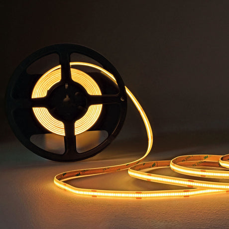 LYYT COBKITWW 24V COB 5m warm white LED tape kit partly unrolled from a black reel, glowing warm amber across a dark surface.