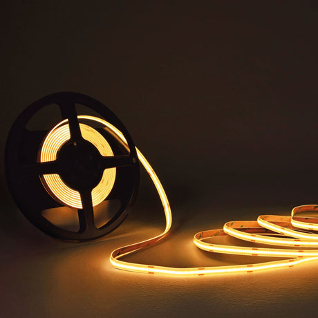 LYYT COBKITWW 24V COB 5m warm white LED tape unspooling from a black reel, glowing in a curved line across a dark surface.