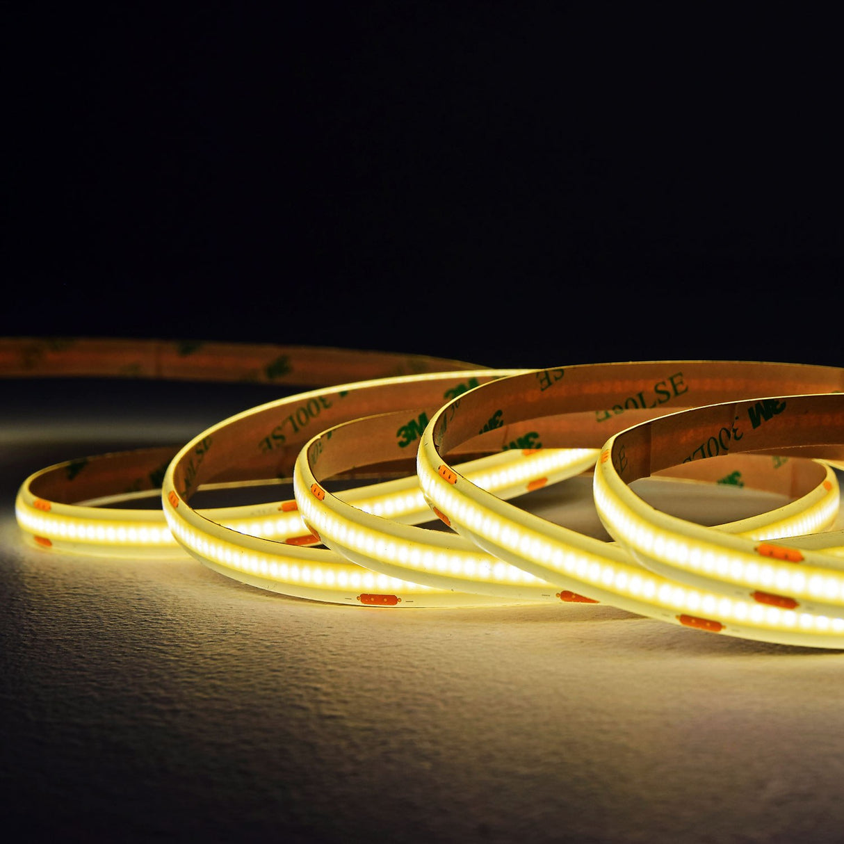 LYYT COBKITNW 24V COB LED tape by AVSL coiled and illuminated in neutral white, showing the slim strip with 3M adhesive backing on a dark surface.