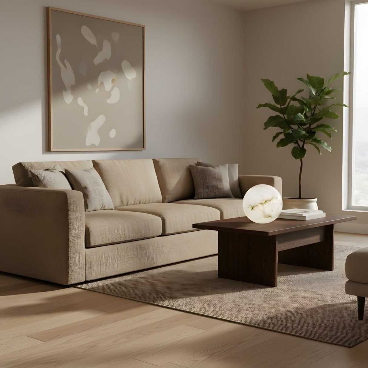 A modern living room with a beige sofa, neutral pillows, a wooden coffee table topped with the Zavero 1 Light Orb Alabaster Table Lamp - Soft White, a large potted plant, abstract wall art, and sunlight on a light wood floor.
