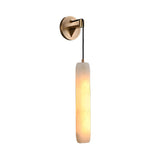 The Elystria LED Vertical Stone Alabaster Wall Light features a round gold brass base and a cylindrical alabaster fixture, suspended by a black cord and glowing softly in warm white.