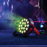 QTX 18x1.5W RGB LED Par Can by AVSL on a stage floor, black housing with 18 LEDs lit yellow-green, red bracket stand, amid haze and coloured lighting.