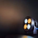 Citronic SilentPAR-200W PAR can by AVSL with four COB LEDs lit in cool and warm white, casting a warm glow on a dark backdrop.