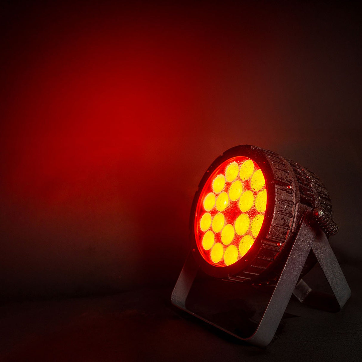 Citronic HIPAR-200 weatherproof RGBLA-UV LED PAR can on floor bracket, glowing yellow with red spill against a dark background.