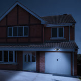LYYT Twin LED PIR Motion Sensor Floodlight in black mounted above a white garage door on a red brick house at night, lighting the driveway.