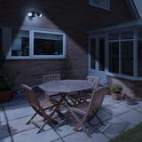LYYT twin LED PIR motion sensor floodlight in black, wall-mounted on a brick house illuminating a patio dining set at night.