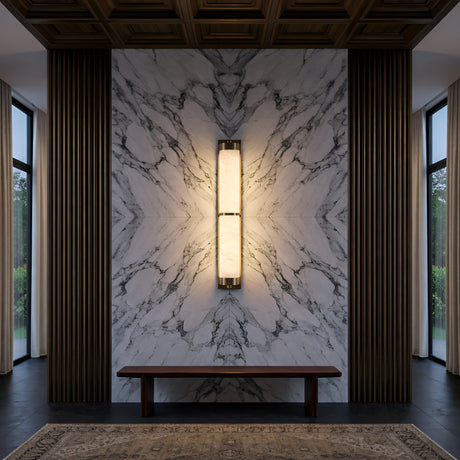 A symmetrical modern interior features a marble accent wall, vertical wooden panels, and a central Arelis LED Linear Alabaster Wall Light in Soft White & Brushed Brass. A simple bench sits below large windows, with part of a rug visible on the floor.