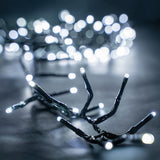 LYYT 960 LED outdoor string lights by AVSL shown lit in cool white, with dark green cable clustered on a grey surface and glowing bokeh behind.