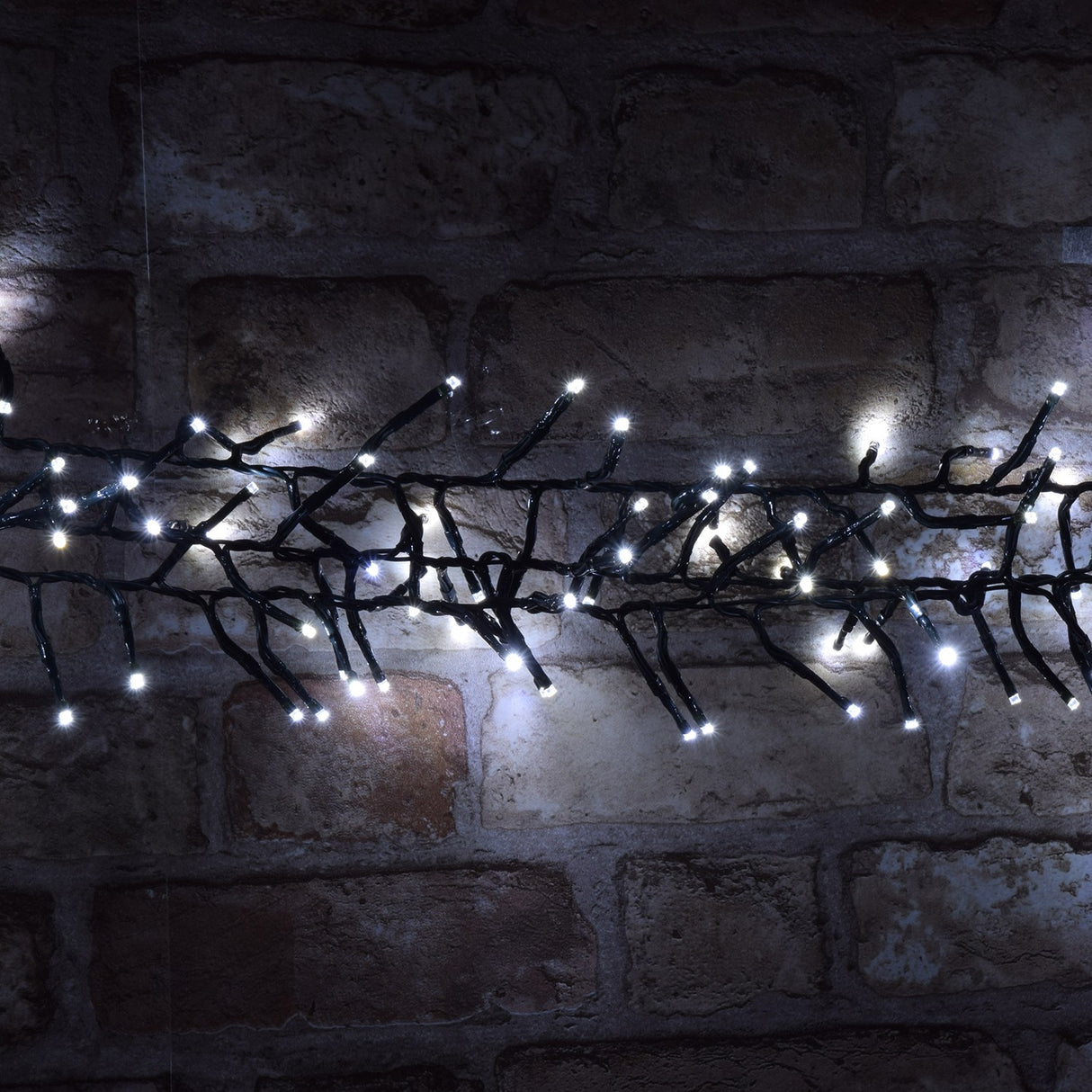 LYYT 960 LED outdoor string lights by AVSL illuminated in cool white along a dark green cable draped across a rustic exposed brick wall at night.