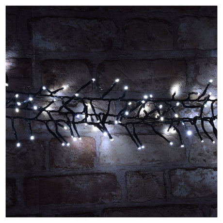 A brick wall is adorned with the LYYT 960 LED Outdoor String Lights in Cool White, featuring small, glowing white bulbs. The lights form a vine-like pattern, casting a soft illumination on the bricks while an energy-saving timer ensures efficient use.