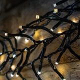 Close-up of LYYT 960 LED outdoor string lights by AVSL, showing clustered warm and cool white LEDs on dark green PVC cable coiled on a stone surface.