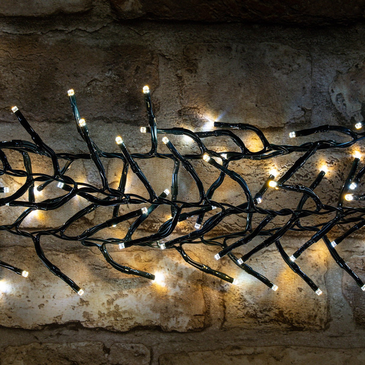 LYYT 960 LED outdoor string lights by AVSL draped against a rustic stone wall, showing clustered warm and cool white LEDs on dark green cable.